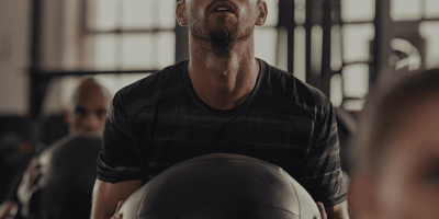 a man holding a medicine ball in a class setting, performing a key component of functional fitness